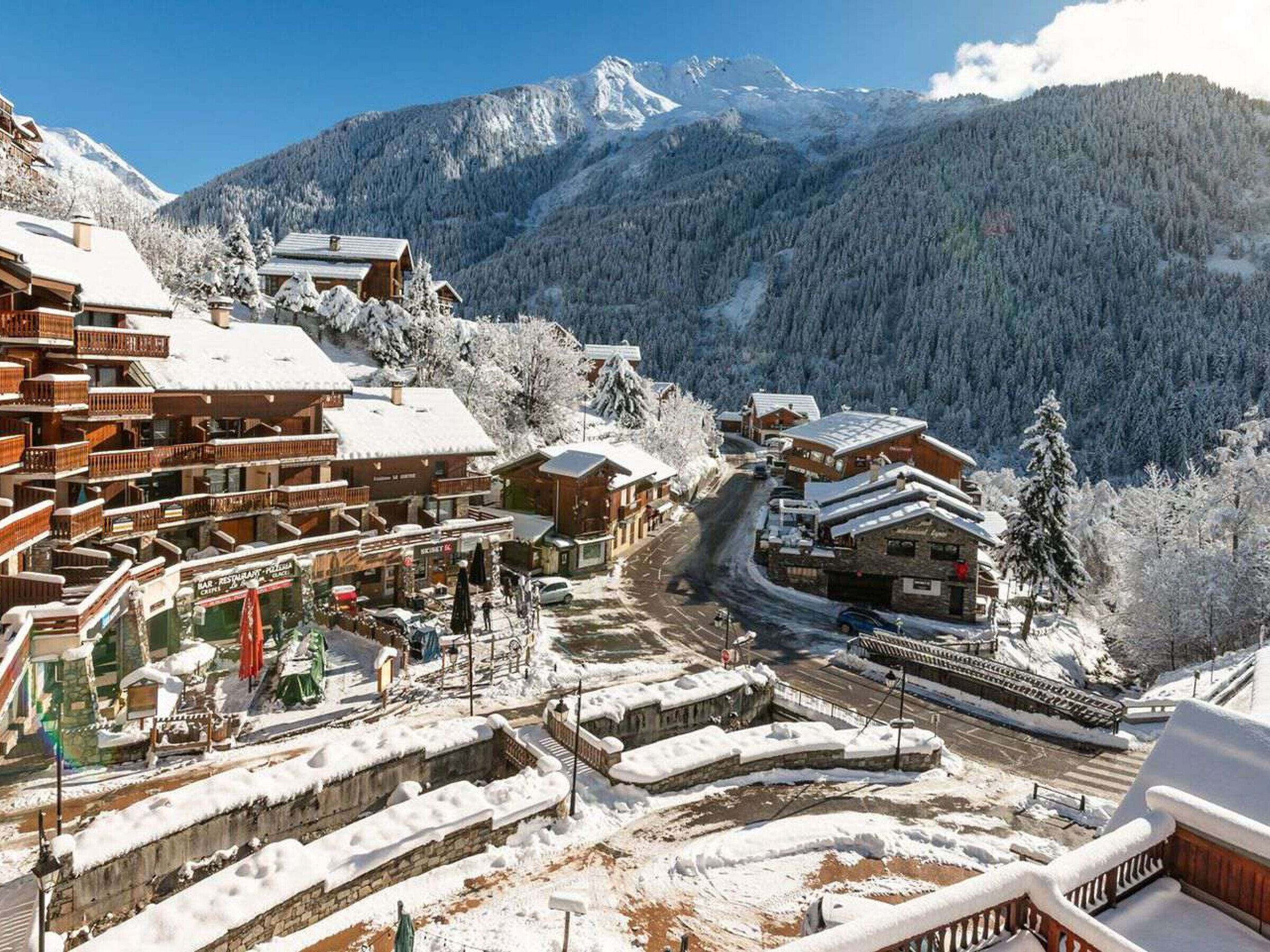 A snow-covered mountain village with wooden buildings, a ski lift, and a clear view of the mountains.