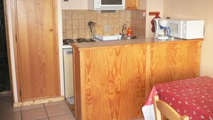 Une cuisine compacte avec des meubles en bois, un four à micro-ondes, une machine à café et un dosseret carrelé.