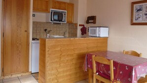 Une cuisine compacte dotée de meubles en bois, d’un four à micro-ondes, d’un petit réfrigérateur et d’une table à manger avec des chaises.