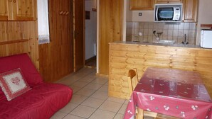Une cuisine compacte avec des meubles en bois, un four à micro-ondes et une petite table à manger recouverte d’une nappe rouge.