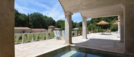 An outdoor swimming pool area with a pergola, lounge chairs, and a view of the surrounding landscape.