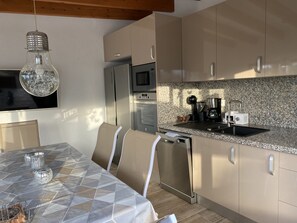 A modern kitchen with stainless steel appliances, a granite countertop, and a dining area with a patterned tablecloth and chairs.
