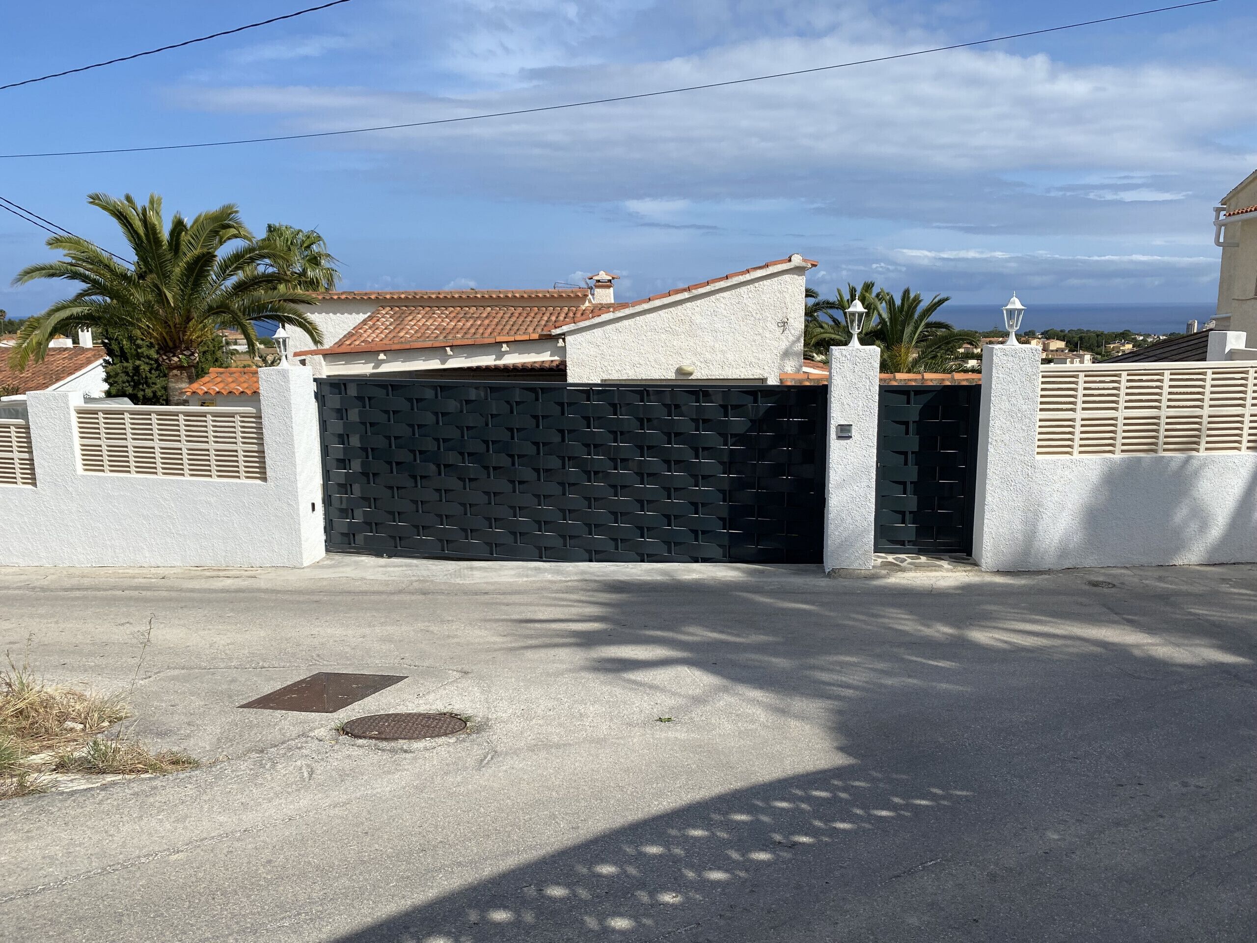 Una zona residencial privada con un portón negro cerrado, paredes blancas y un techo de tejas.