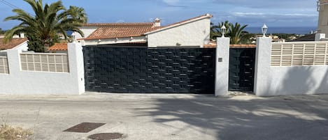 Uma área residencial murada com um portão preto fechado, paredes brancas e um telhado telhado.