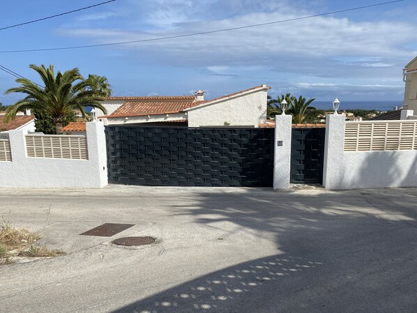 A gated residential area with a closed black gate, white walls, and a tiled roof.