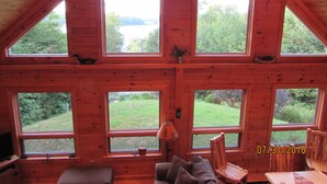 A cabin with multiple large windows offering views of a green landscape and a body of water.