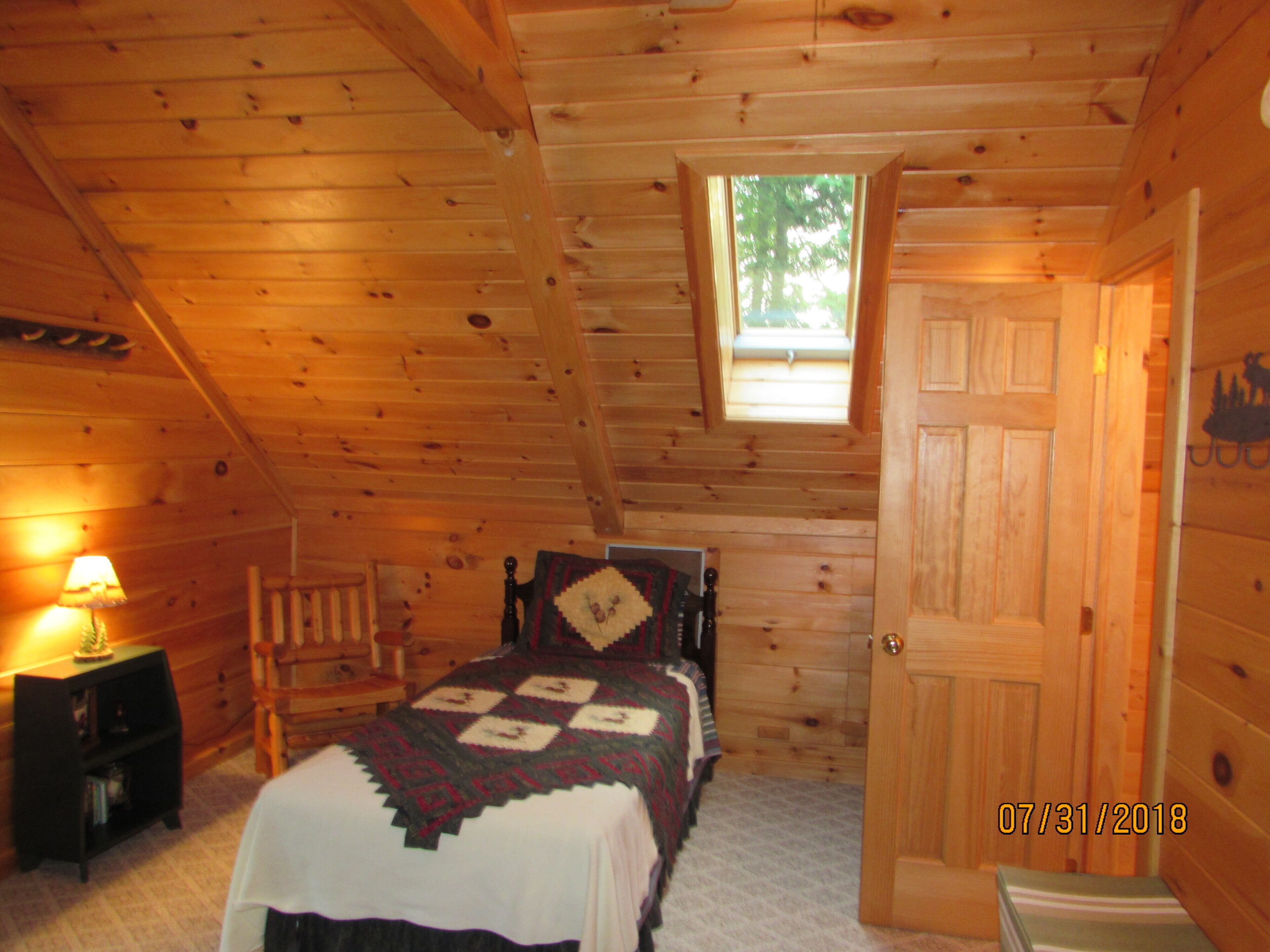 Une chambre confortable, aménagée dans un chalet en bois, avec un lit, une table de chevet, une lampe et une fenêtre.