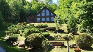 A log cabin with a large window, surrounded by lush greenery and a sign indicating a bear sighting area.