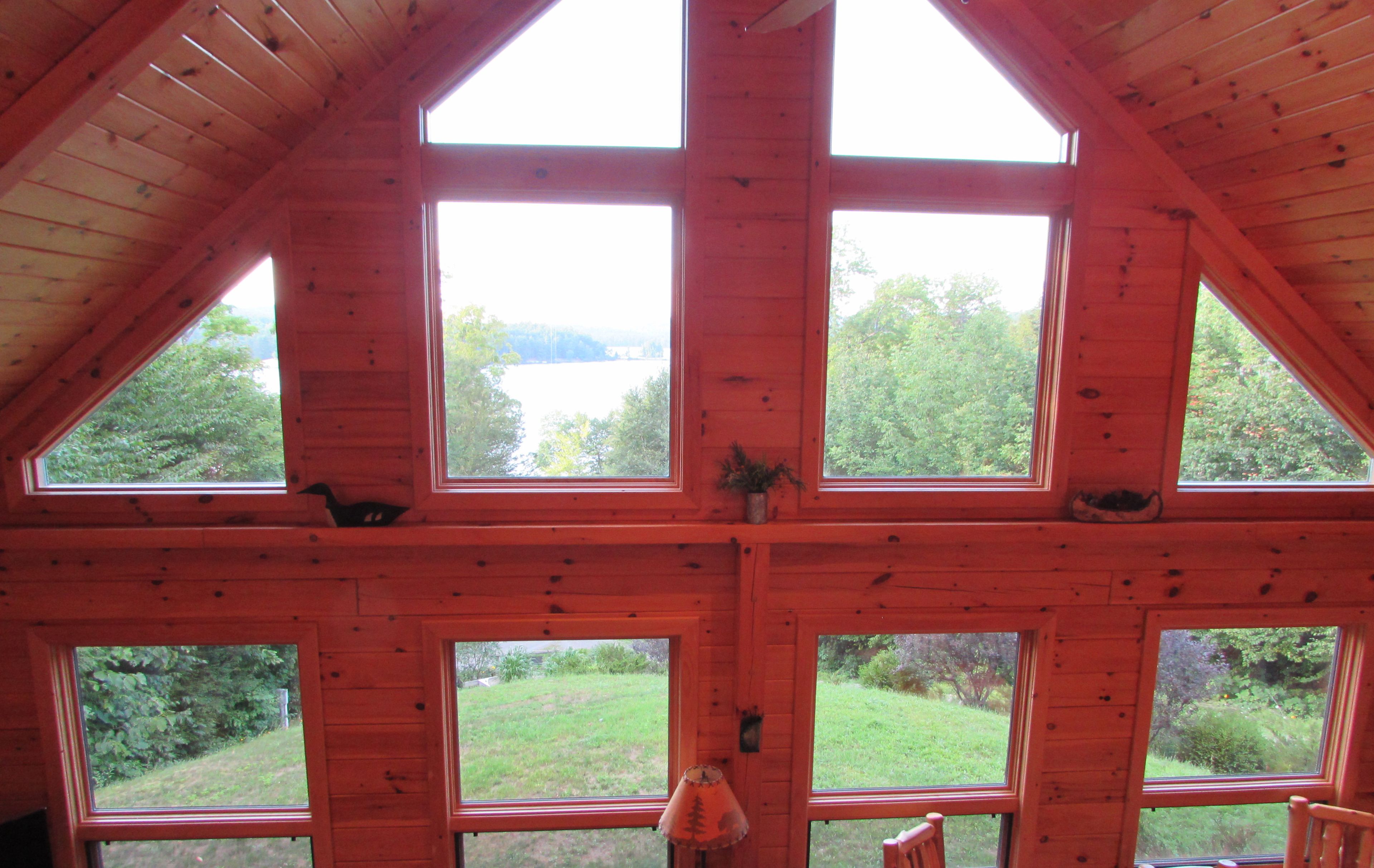 Une cabane dotée de nombreuses grandes fenêtres offrant une vue sur un paysage verdoyant et une étendue d’eau.