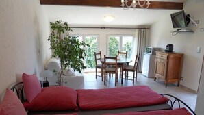 Une pièce comprenant un lit, une table à manger avec des chaises, un téléviseur et une plante.