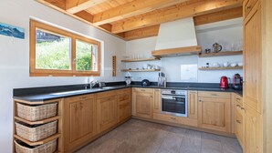 A kitchen with wooden cabinets, a black countertop, a window, and a built-in oven. - Ann - SUNNY & LUXE chalet 8 pers (Haute-Nendaz)