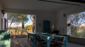 A dining area with a long table and chairs, a stone floor, and a view of trees and hills through large windows. - Sughera - Share-croppers house (Impruneta)