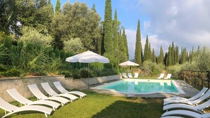 A swimming pool with white lounge chairs and umbrellas, surrounded by greenery and tall trees. - Sughera - Share-croppers house (Impruneta)