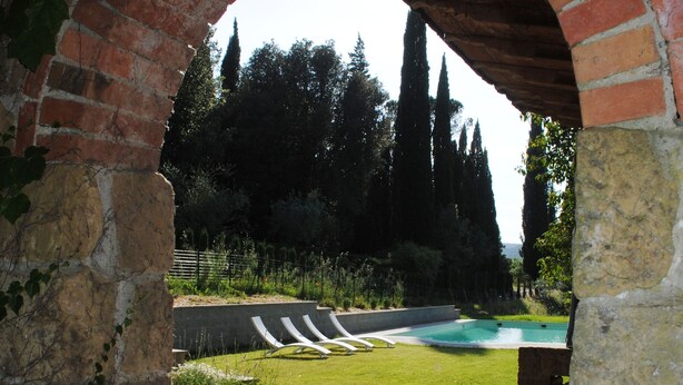 An arched stone structure leading to a pool area with a paved path and greenery. - Sughera - Share-croppers house (Impruneta)