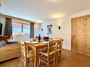 Un coin repas avec une table en bois dressée pour quatre personnes, entourée de chaises, d’un canapé et d’une fenêtre agrémentée de rideaux.