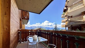 A balcony with a table and chairs, a wooden railing, and a view of snow-capped mountains. - Pracondu 1 107 - OUTDOOR & FUN  charming apartment (Haute-Nendaz)