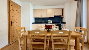 A dining area with a wooden table and chairs, a kitchen in the background, and a wooden door. - Pracondu 1 107 - OUTDOOR & FUN  charming apartment (Haute-Nendaz)
