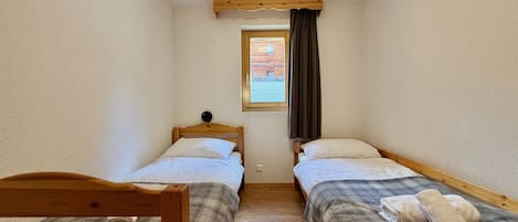 Una habitación estrecha con dos camas de madera, una ventana con cortinas y una viga de madera en el techo.