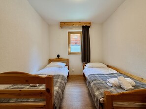 Ein schmaler Raum mit zwei Holzbettgestellen, einem fenster mit Vorhängen und einem Holzbalken an der Decke.
