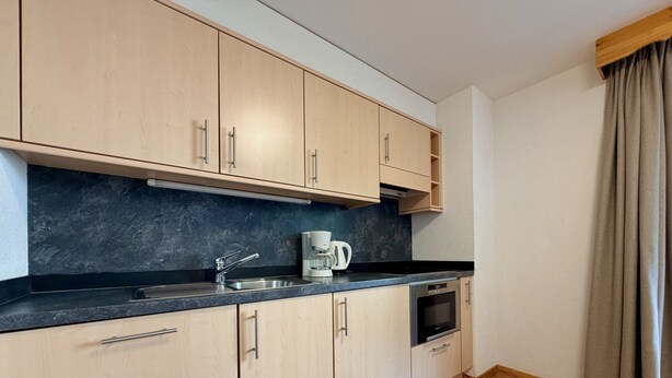 A compact kitchen with light wood cabinets, a black countertop, a coffee maker, a microwave, and a built-in oven. - Pracondu 1 107 - OUTDOOR & FUN  charming apartment (Haute-Nendaz)