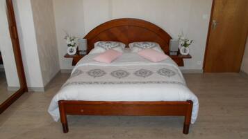 Quarto com cama de madeira, duas mesas de cabeceira com abajures e um espelho na parede esquerda.