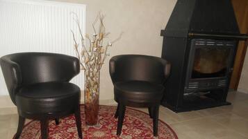 Deux fauteuils noirs, un tapis aux motifs rouges et dorés et une cheminée.
