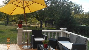An outdoor patio with wicker furniture, a yellow umbrella, and a view of a garden. - Bed & Breakfast (Villers-Sur-Port)
