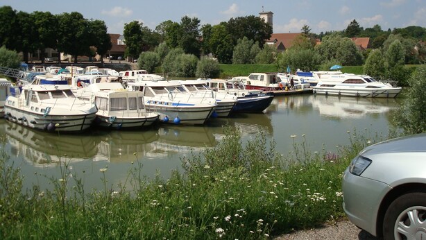 A marina with several boats docked, surrounded by greenery and a church in the background. - Bed & Breakfast (Villers-Sur-Port)