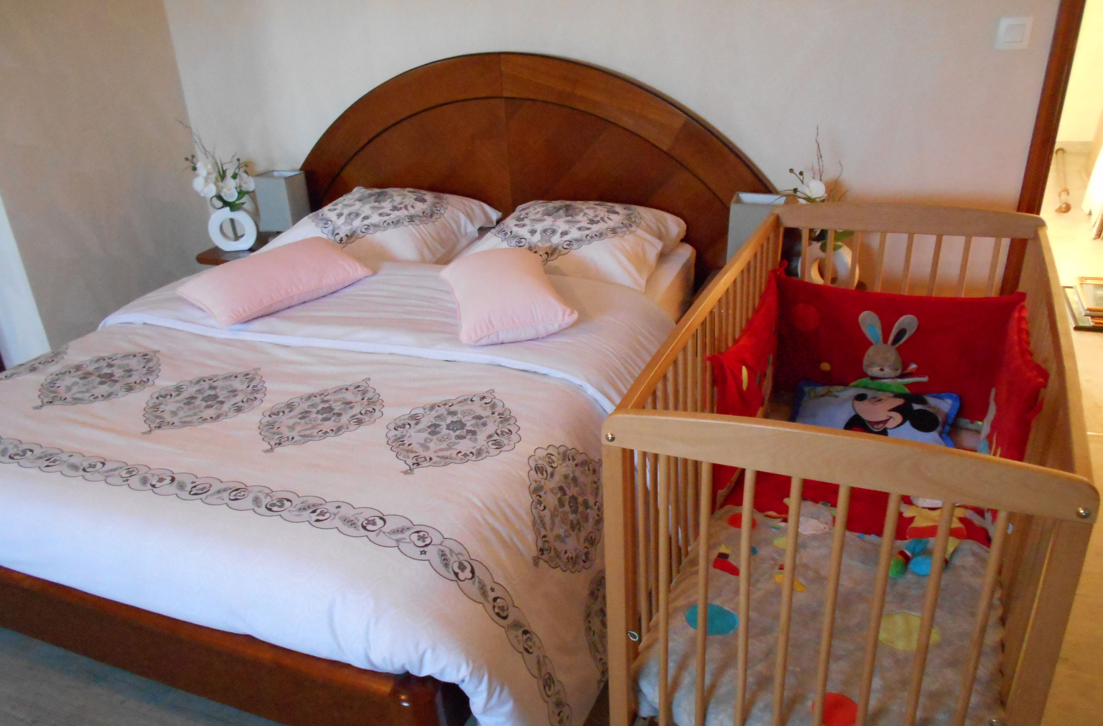 Un dormitorio con una cama de madera, una cuna con un cojín de Mickey Mouse y una mesita de noche con un florero.
