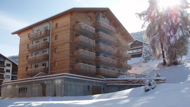 Un bâtiment en bois à plusieurs étages, doté de balcons, entouré d’un paysage enneigé et d’arbres.