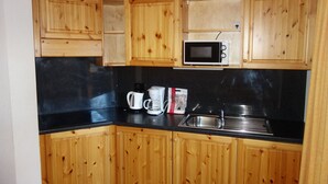 Une cuisine avec des meubles de rangement en bois, un plan de travail noir, un four à micro-ondes, une machine à café et une bouilloire.