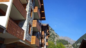 A multi-story building with balconies, stone walls, and a mountainous backdrop.