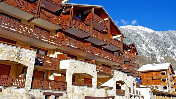 A multi-story building with wooden balconies and stone walls, set against a snowy mountain backdrop.