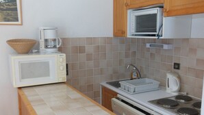 A compact kitchen with a microwave, coffee maker, kettle, and a dishwasher.