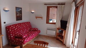 A cozy living room with a red patterned sofa, a wooden table, and a television.