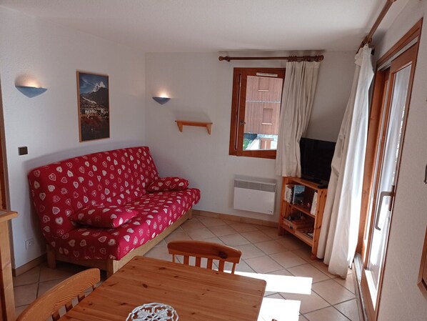 Een knusse woonkamer met een rode sofa met patroon, een houten tafel en een televisie.