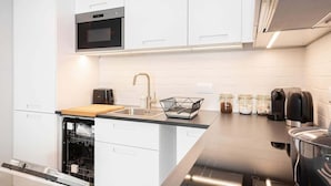 A modern kitchen with white cabinets, a built-in oven, a dishwasher, a stainless steel countertop, a sink, and a coffee maker.