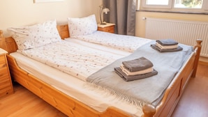 Un lit double avec une literie à motifs floraux, une table de chevet, une lampe et une vue sur l’extérieur par une fenêtre.