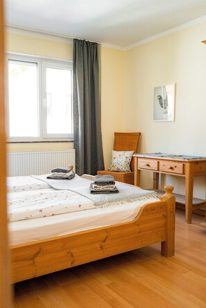 Une chambre à coucher avec un lit en bois, une chaise, un bureau et une fenêtre avec des rideaux.