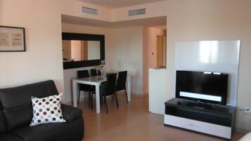 Un salon moderne avec un canapé noir, une table basse blanche, un téléviseur à écran plat et un coin repas comprenant une table blanche et des chaises noires.