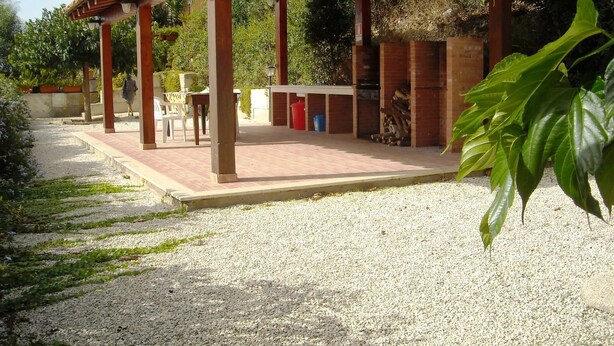 Uma área de estar coberta ao ar livre, com churrasqueira, mesas e cadeiras.