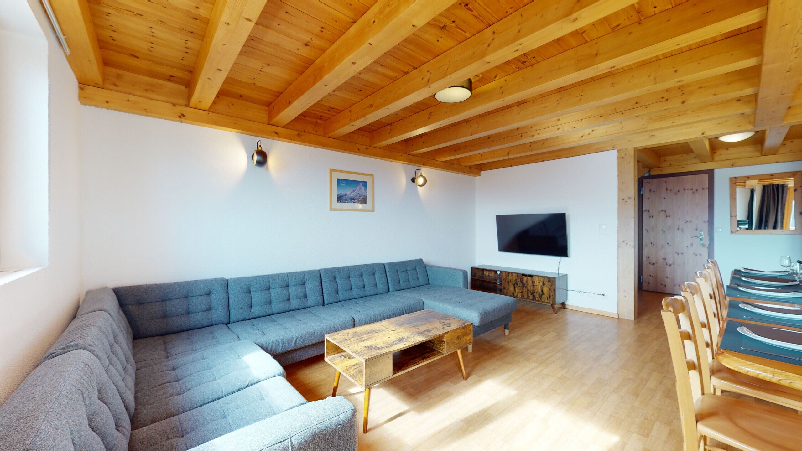 Un salon comprenant un canapé d’angle, une table basse en bois et un téléviseur à écran plat fixé au mur.