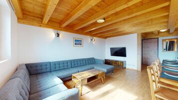Un salon comprenant un canapé d’angle, une table basse en bois et un téléviseur à écran plat fixé au mur.