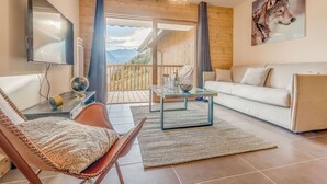Un salon moderne avec un canapé, une table basse en verre, un fauteuil, un téléviseur et un tableau représentant un loup.