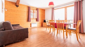 Une pièce avec un mur en bois, un canapé, une table à manger avec des chaises et un luminaire suspendu rouge.