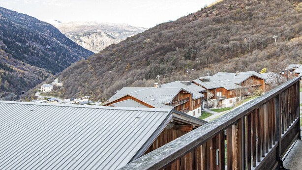Un balcon en bois offrant une vue sur un paysage montagneux et sur plusieurs bâtiments.