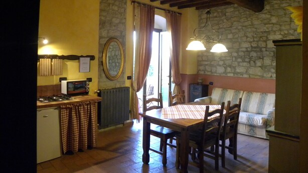A rustic kitchen with a stone wall, wooden beams, a dining table with chairs, and a stone fireplace. - Country Resort Rubino with shared swimming pool  (Rignano sull'Arno)