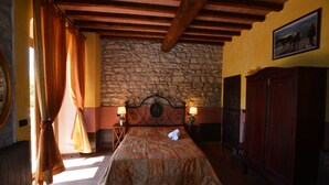 A bedroom with a stone wall, wooden ceiling beams, a bed with a quilt, two bedside lamps, and a wooden wardrobe. - Country Resort Rubino with shared swimming pool  (Rignano sull'Arno)