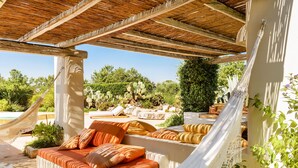 A covered outdoor seating area with a hammock, cushioned seating, and a view of a pool and desert landscape. - Luxury villa for 6 people with salt pool and in the middle of 14,000sqm  (Ostuni)