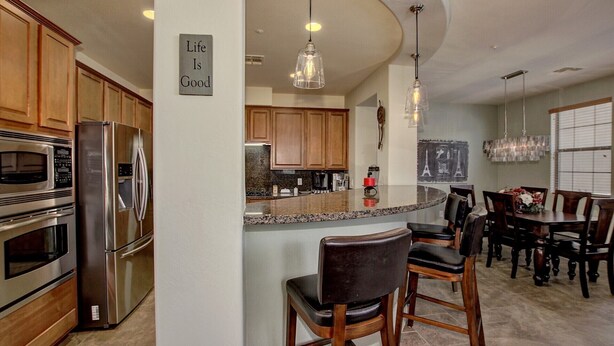 A modern kitchen with stainless steel appliances, a central island with bar stools, and a sign stating "Life Is Good".